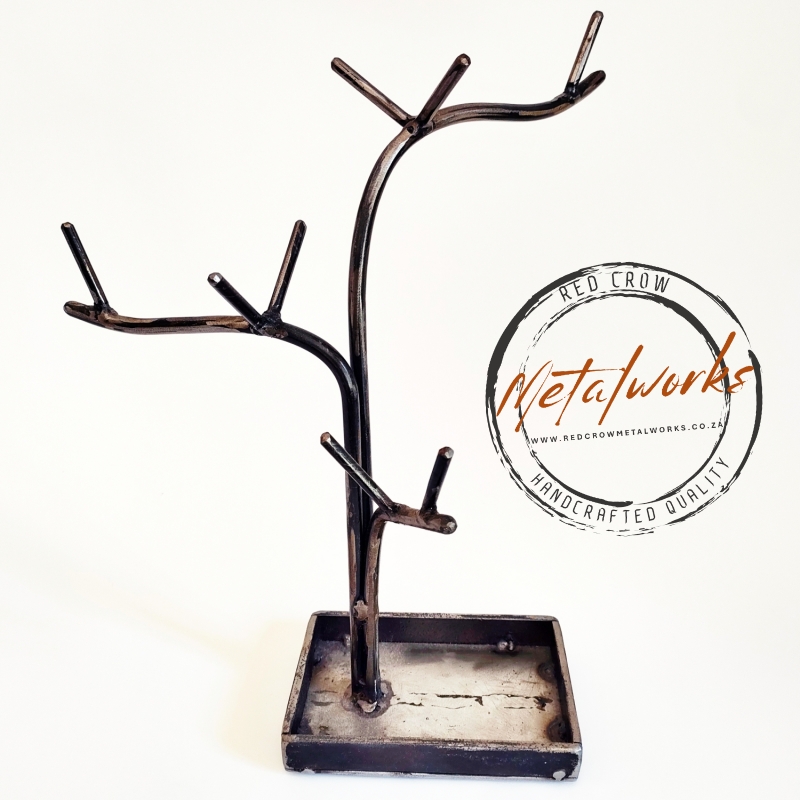 Side profile of a sculptural jewellery stand made from natural-finish mild steel, featuring organic branches for necklaces and a base tray with a clear-coated finish