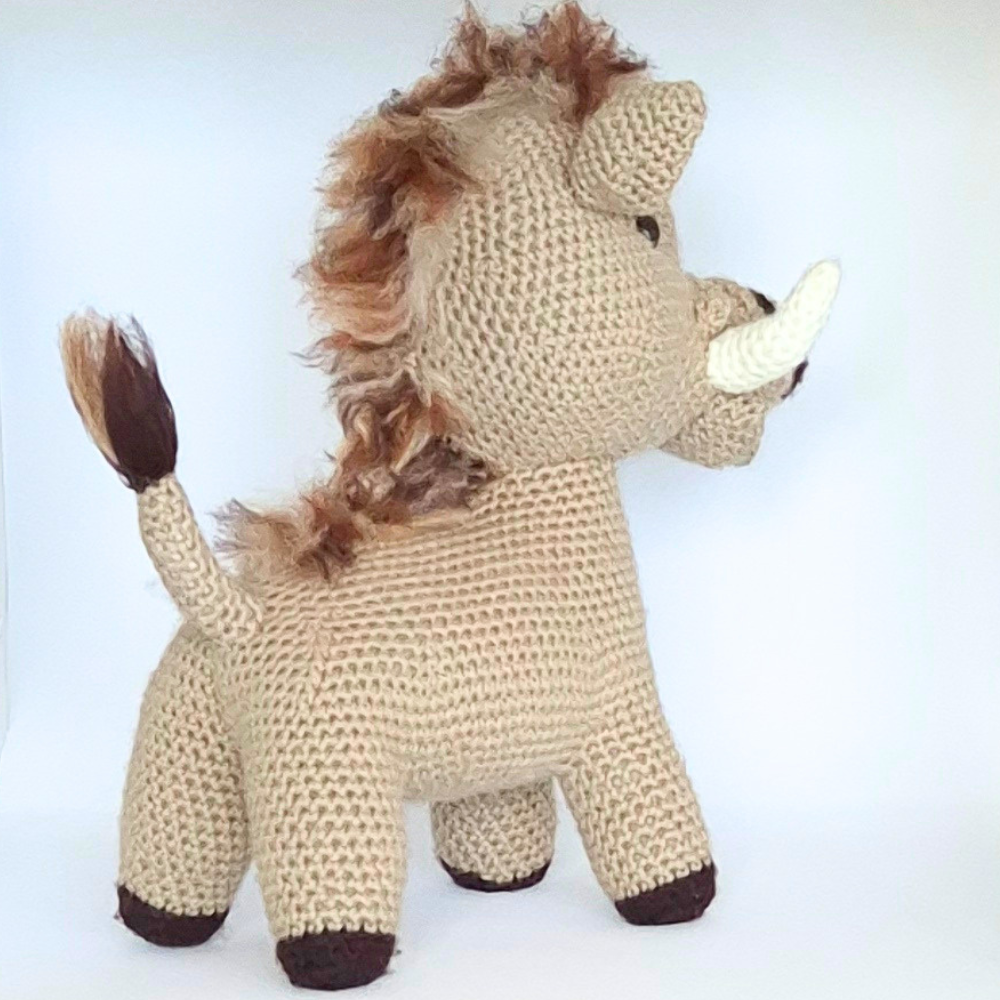 Handmade crochet plush toy, African inspired warthog with beige body, dark hooves and nose, white tusks and a fluffy mane, standing upright with detailed features